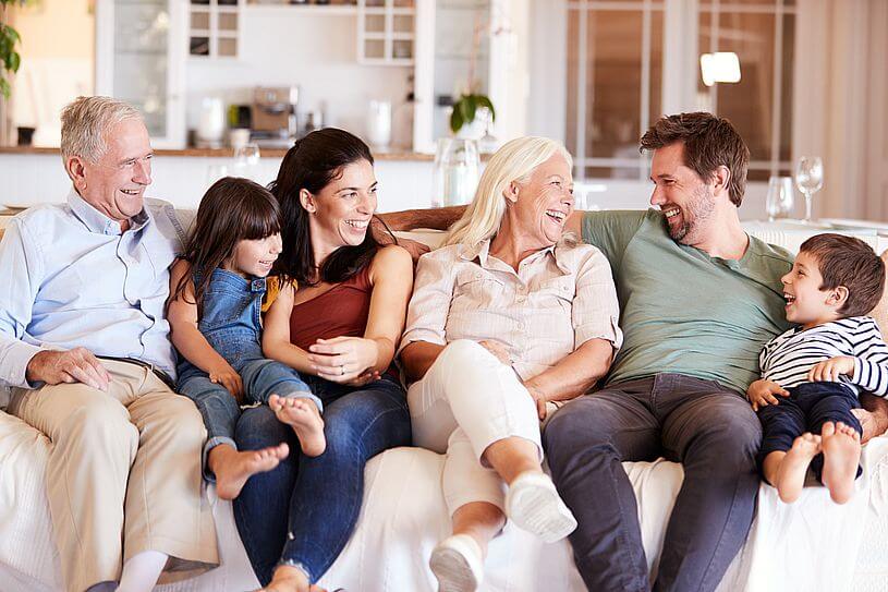 Aplikacja Bezpieczna Rodzina, czyli dziadkowie, rodzice i dzieci siedzą na sofie w salonie i uśmiechają się do siebie