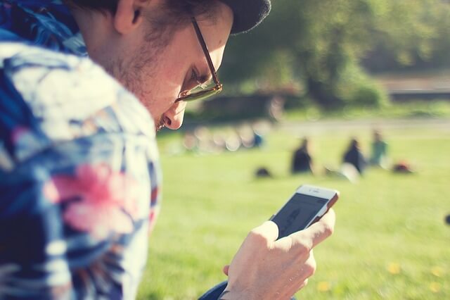 młody ojciec w okularach przeciwsłonecznych siedzi w parku i dzwoni na smartwatch z kartą sim swojego dziecka