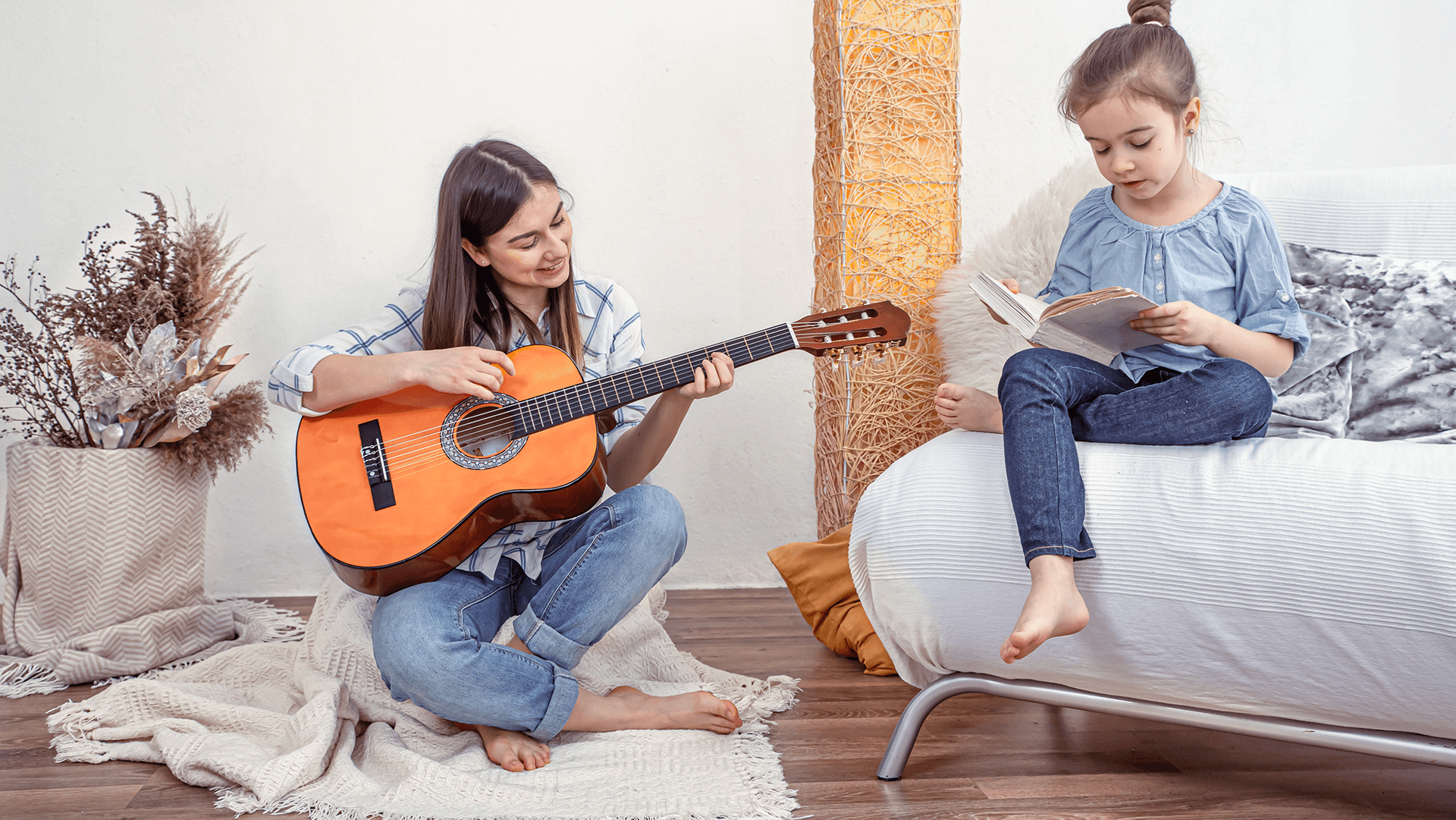 Dziewczynka siedząca na podłodze z gitarą, grająca swojej młodszej siostrze, siedzącej obok na białej kanapie