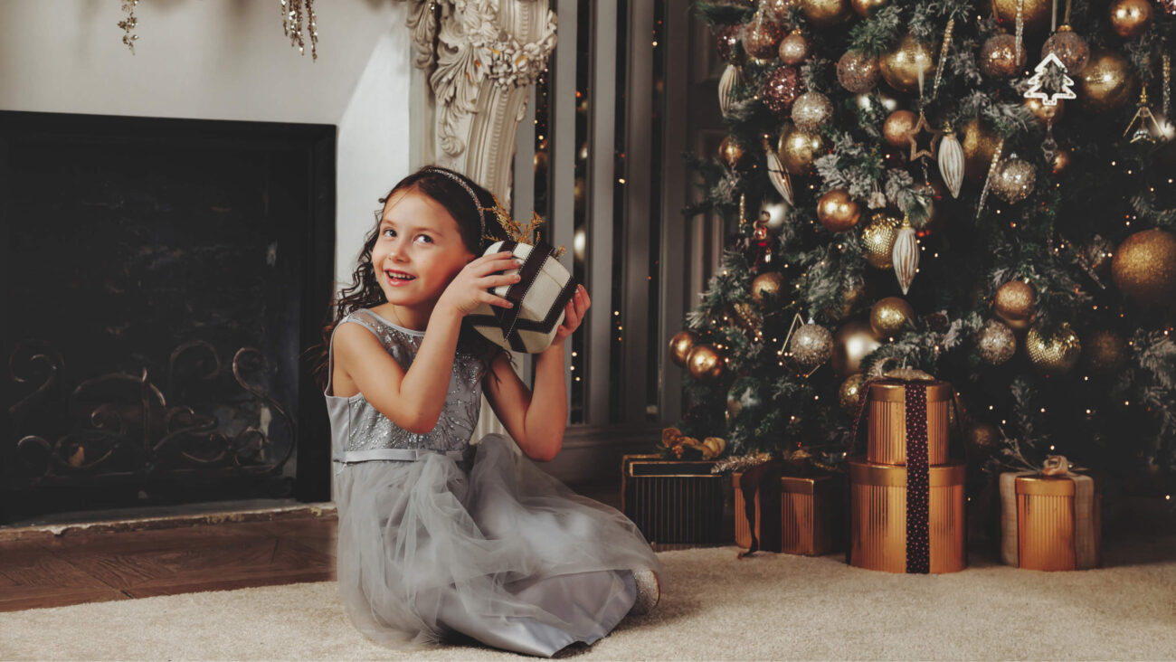 Dziewczynka siedząca na podłodze przy choince z prezentem